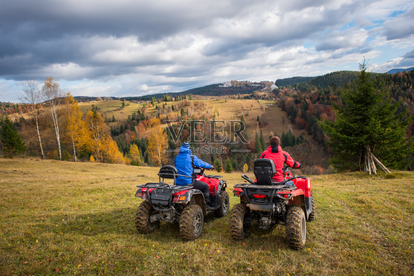 两名男子坐在四轮自行车欣赏美丽的风景山和五颜六色的森林下的天空积云在秋天照片摄影图片