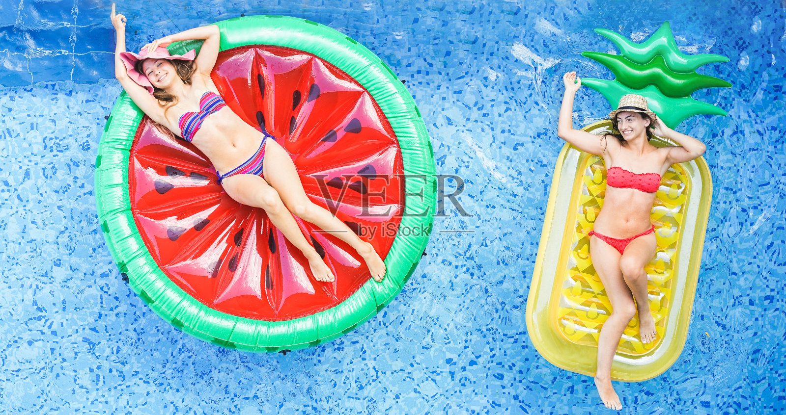 快乐的女孩漂浮在游泳池里的热带水果lilos -年轻的女性朋友放松在度假酒店的暑假-旅游，寒冷，假期，青年概念-温暖过滤器照片摄影图片