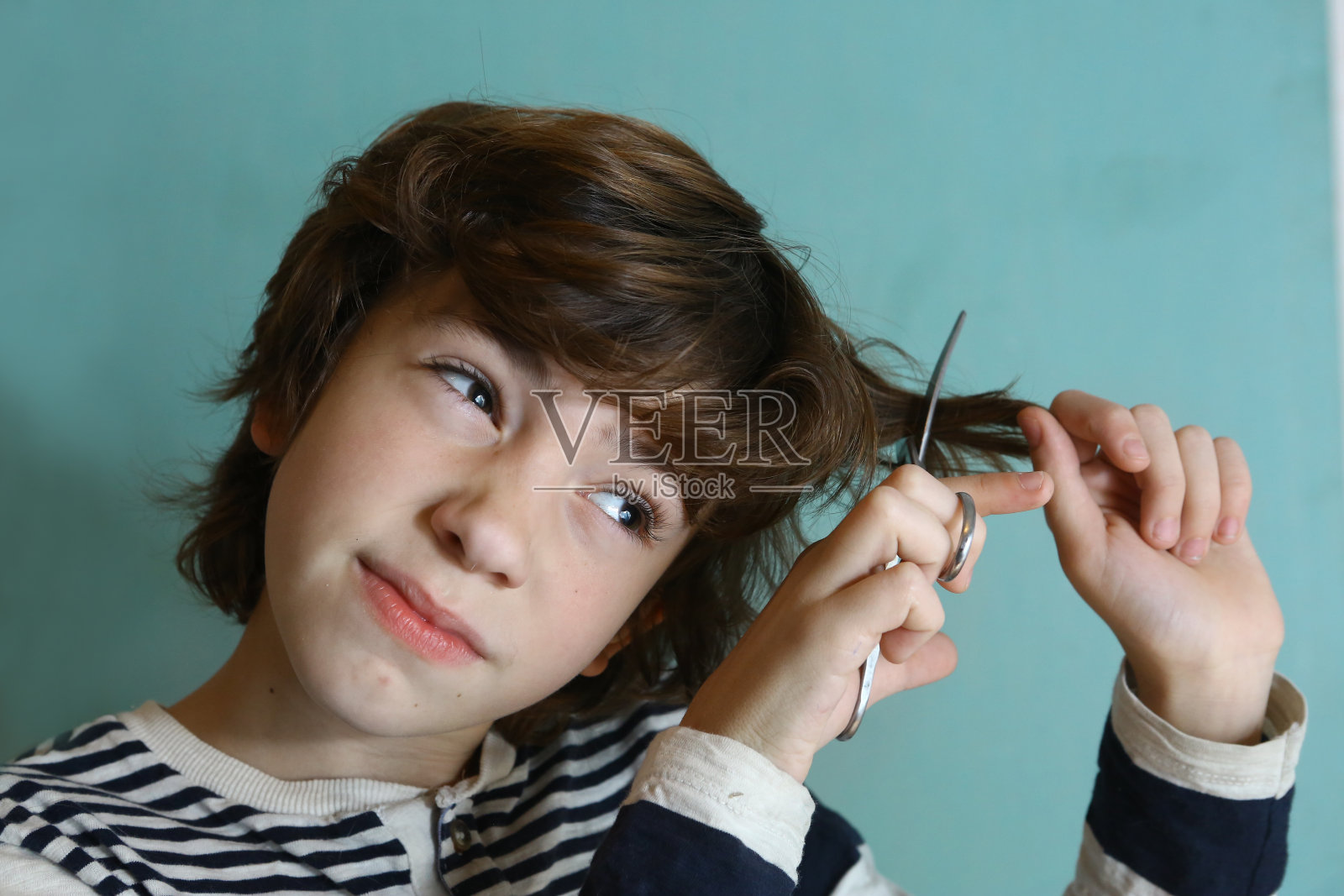 一个十几岁的男孩用剪刀剪头发照片摄影图片