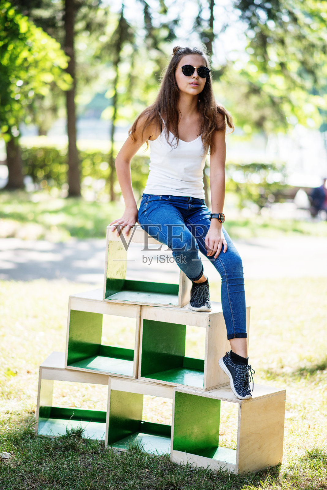 一个阳光明媚的日子里，一个穿着时尚的女孩在公园的木箱上摆姿势照片摄影图片