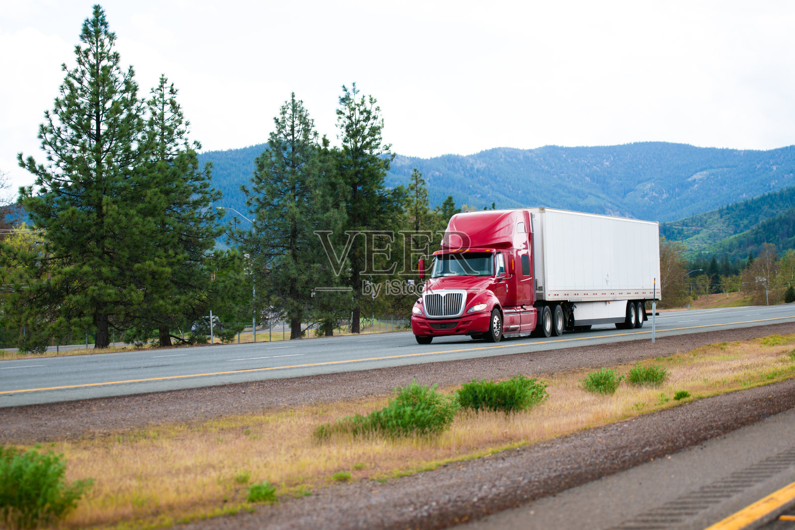 红色现代半挂车与干式货车拖车行驶在分割的I-5公路在加利福尼亚照片摄影图片