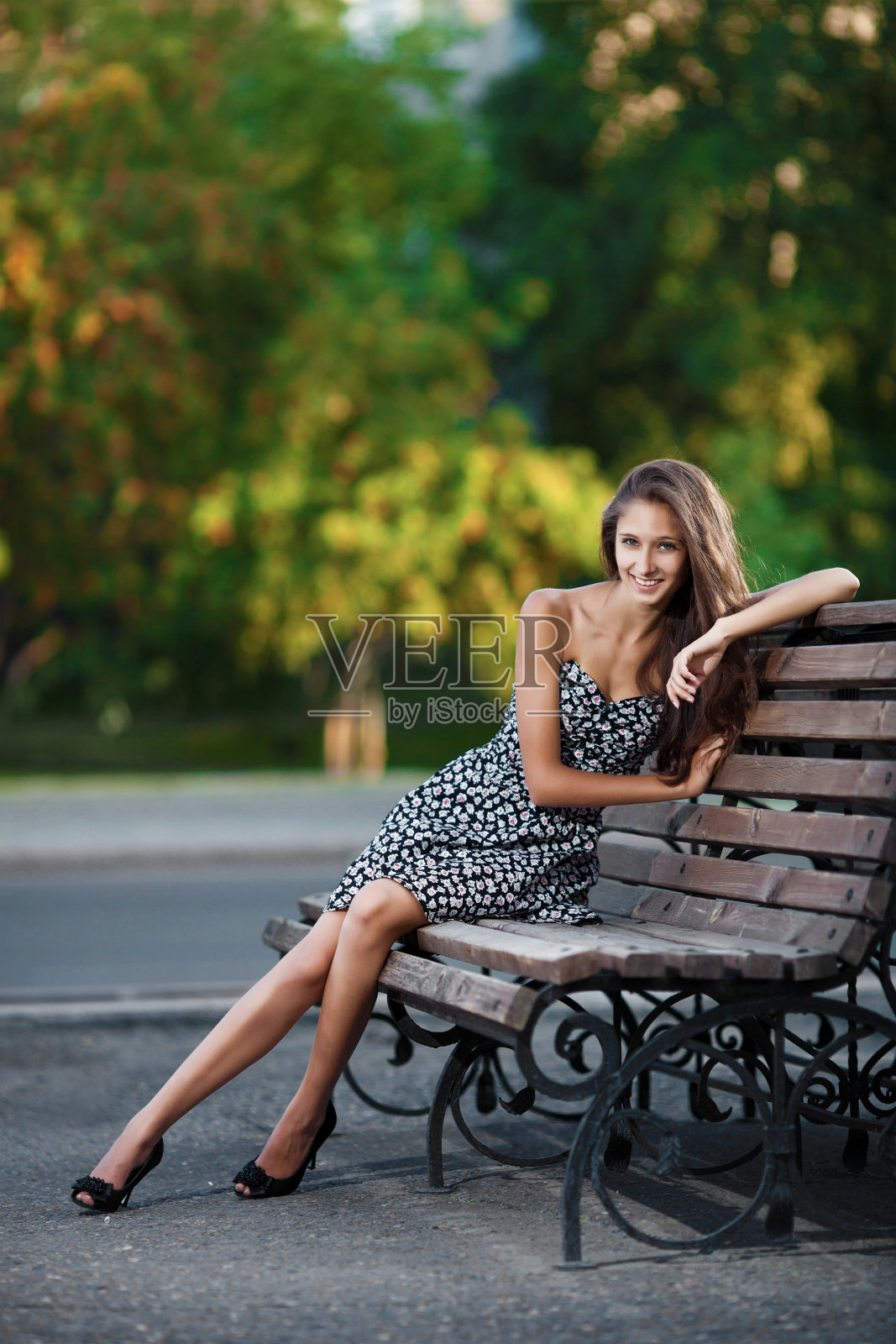 漂亮的黑发女子坐在长凳上。城市背景照片摄影图片