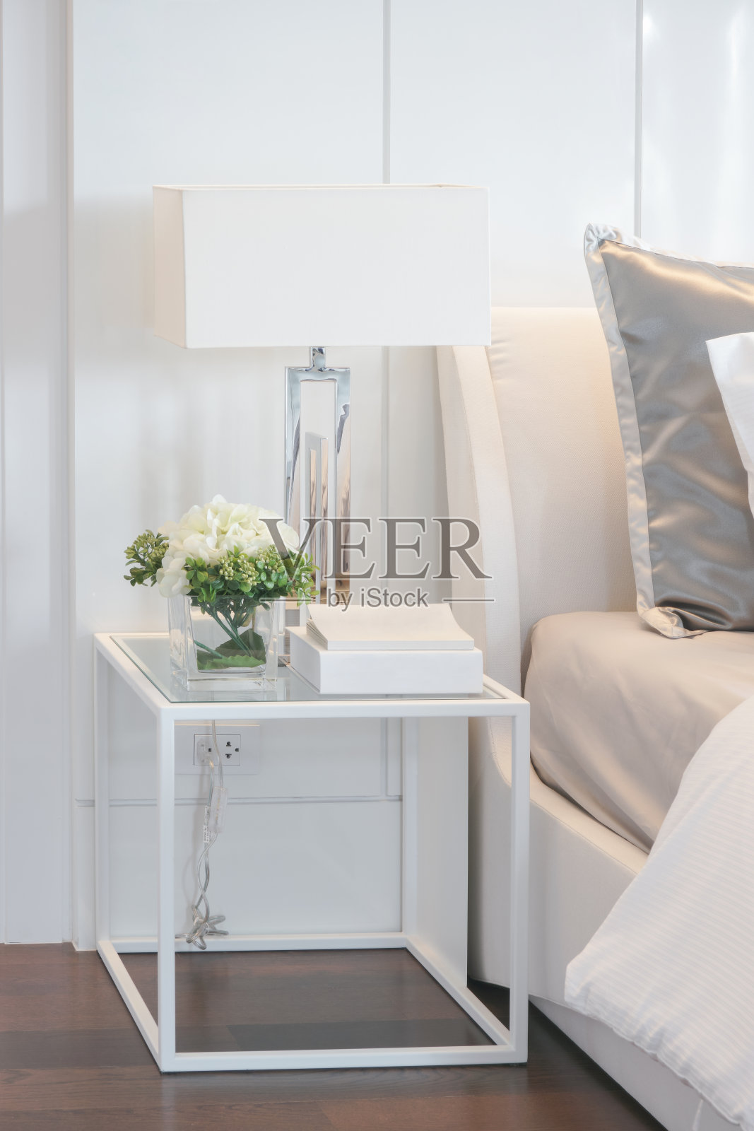现代室内卧室中，白色框架床头柜上放着花瓶、书籍和阅读灯照片摄影图片