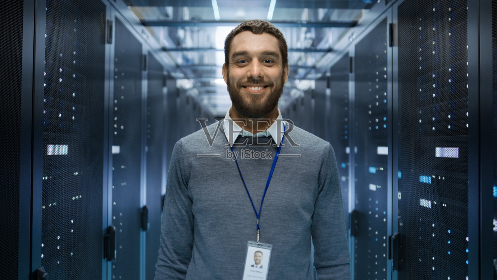一个古玩，积极和微笑的IT工程师站在一个大数据中心服务器室中间的肖像。照片摄影图片
