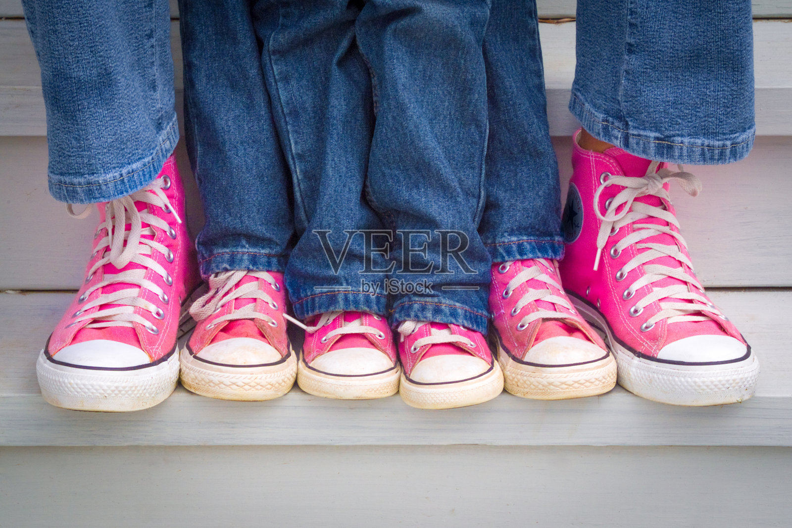 一位母亲和她的两个女儿炫耀她们的粉色运动鞋。照片摄影图片
