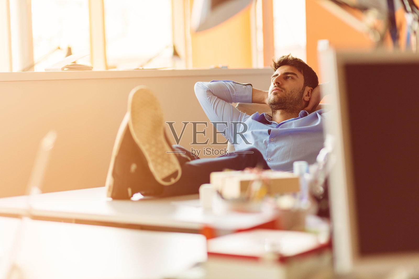 一个白种商人坐在办公室里，双手放在脑后做白日梦。照片摄影图片
