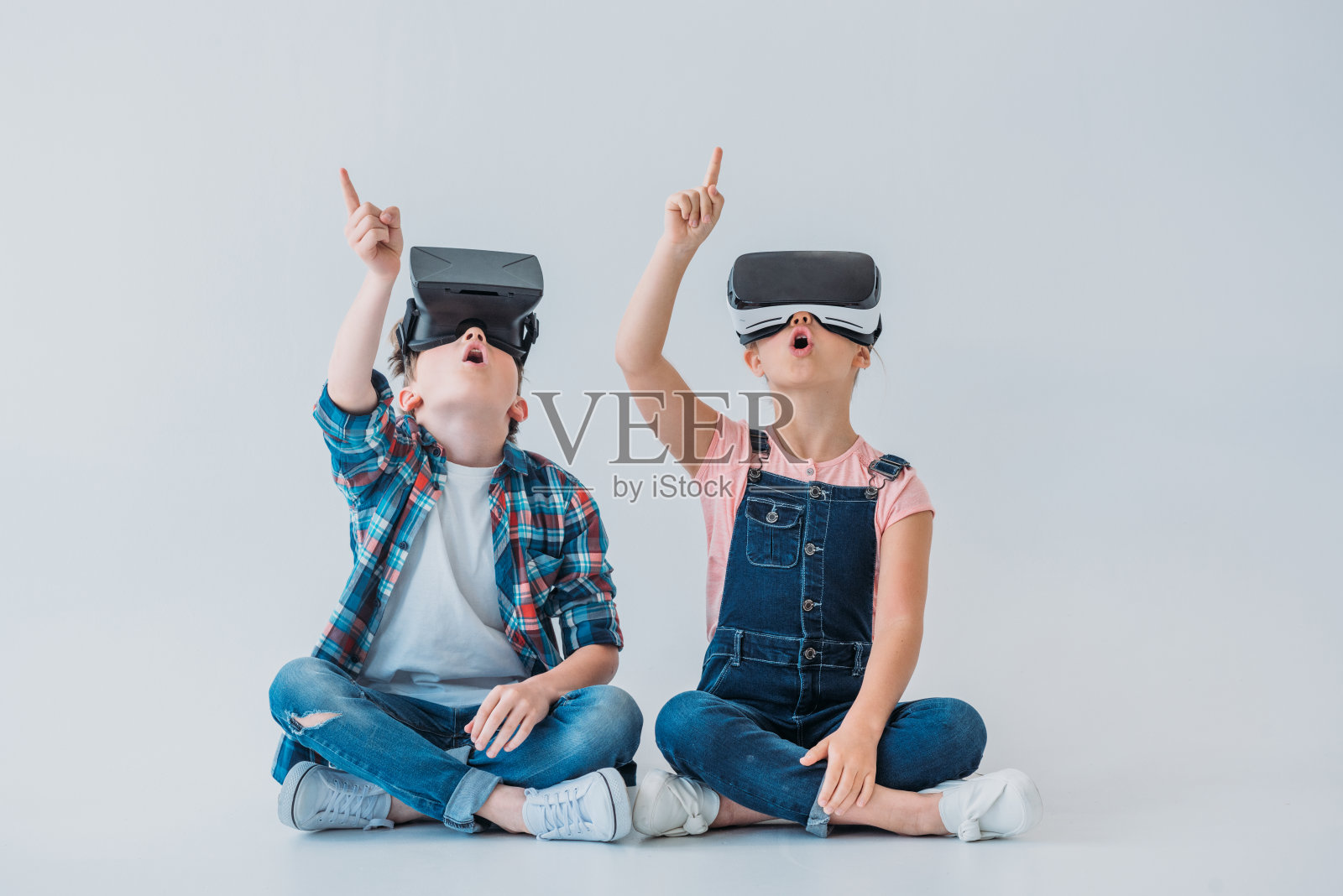 孩子们坐在地板上，戴着虚拟现实头盔，用手指向上指照片摄影图片