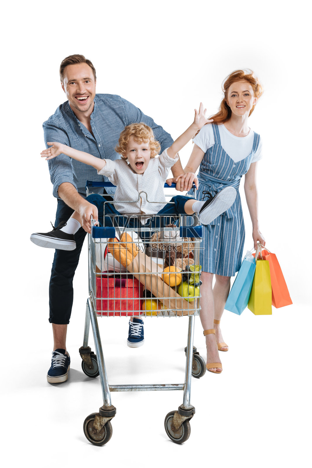快乐的年轻父母拿着纸袋，带着快乐的小儿子坐在购物车里照片摄影图片