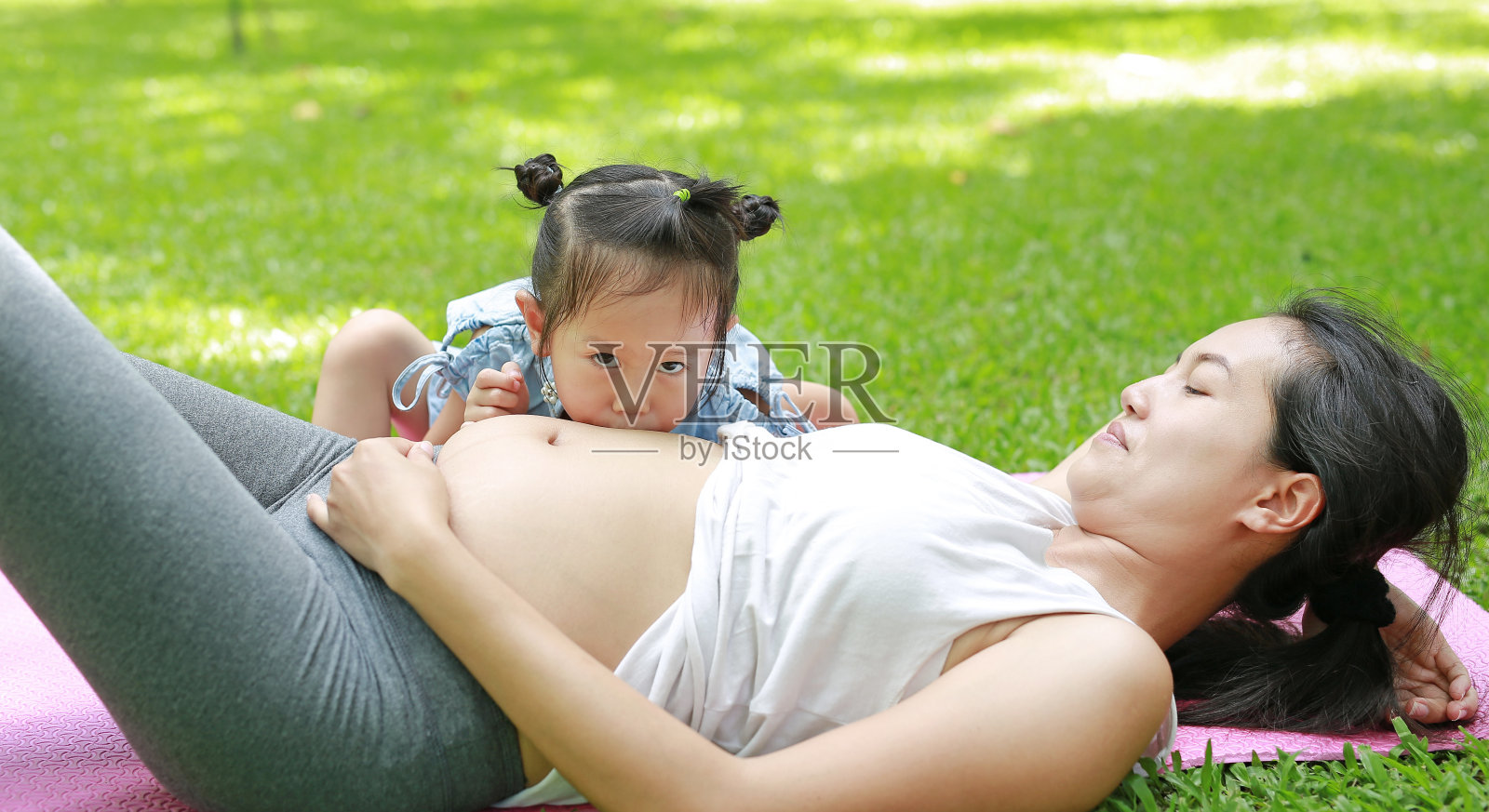 快乐的孩子在花园里亲吻孕妇的肚子。照片摄影图片