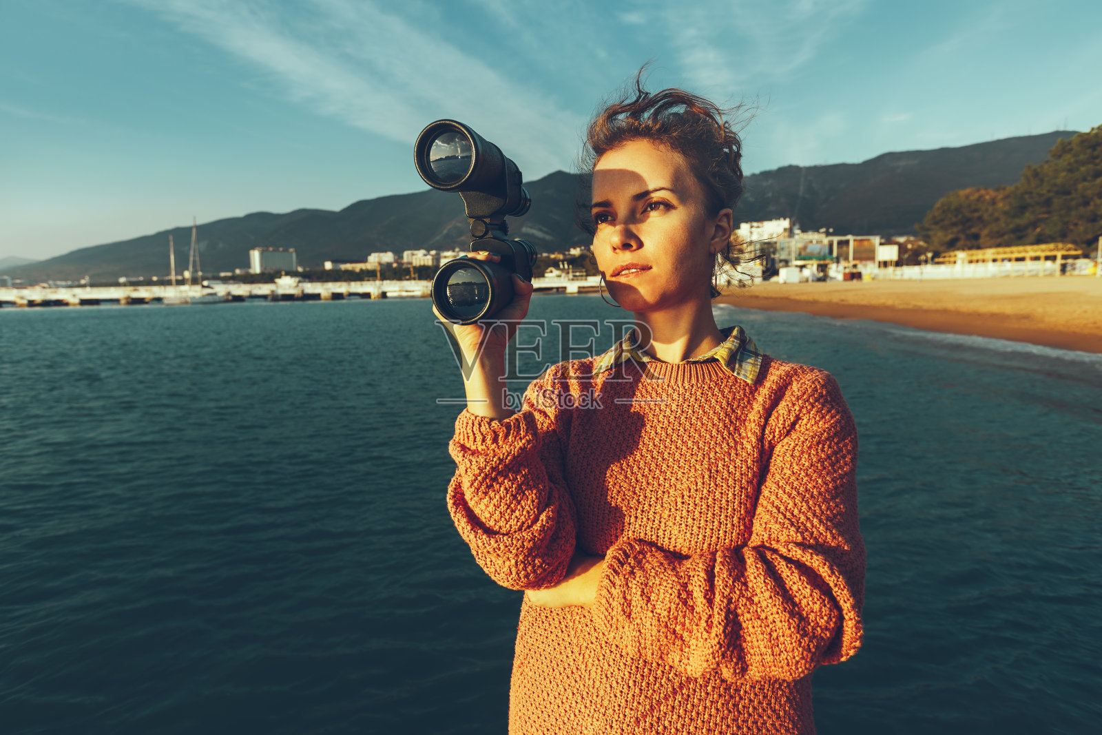 美丽的年轻女子手拿望远镜站在海边欣赏大自然照片摄影图片