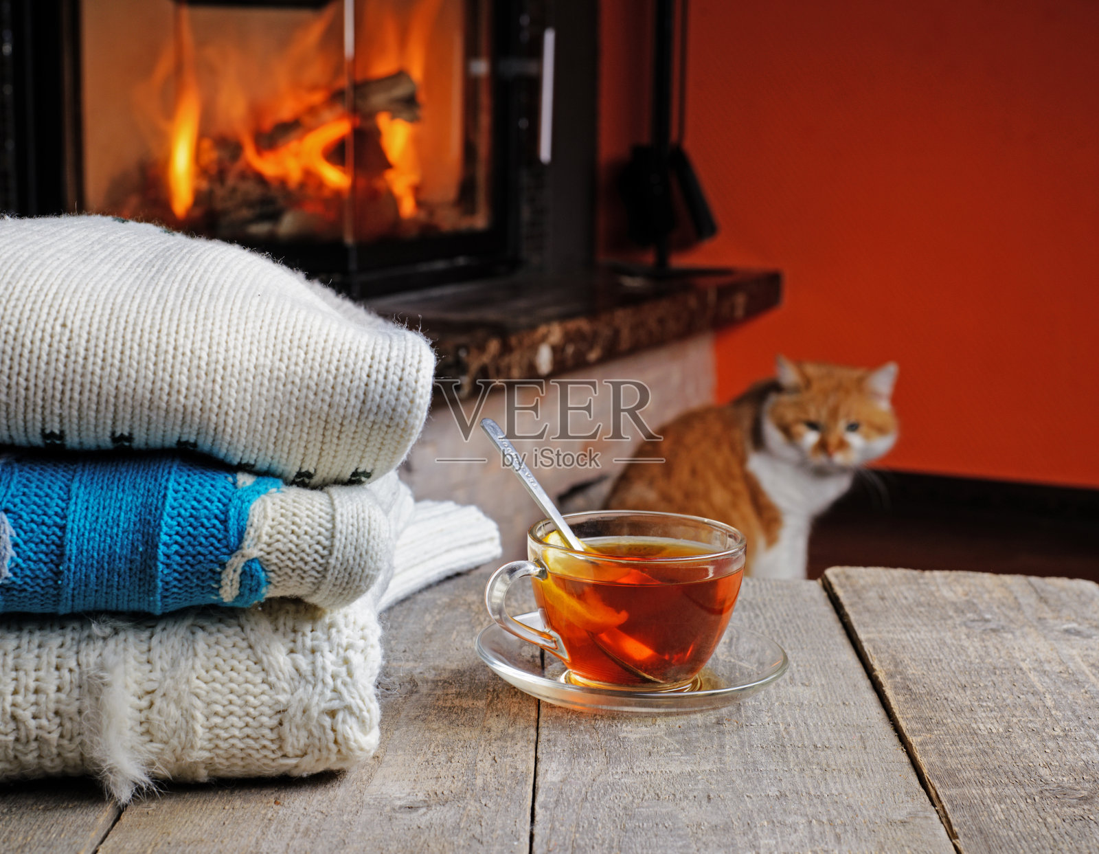 一堆舒适的针织毛衣，一杯带柠檬的热茶放在旧木桌上，旁边是燃烧着的壁炉，猫坐在后面照片摄影图片