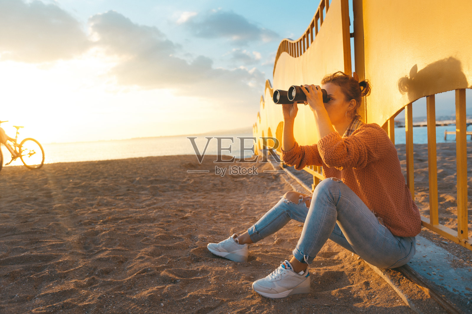 年轻美丽的女孩坐在海滩上，用双筒望远镜看。旅游假期旅游概念照片摄影图片