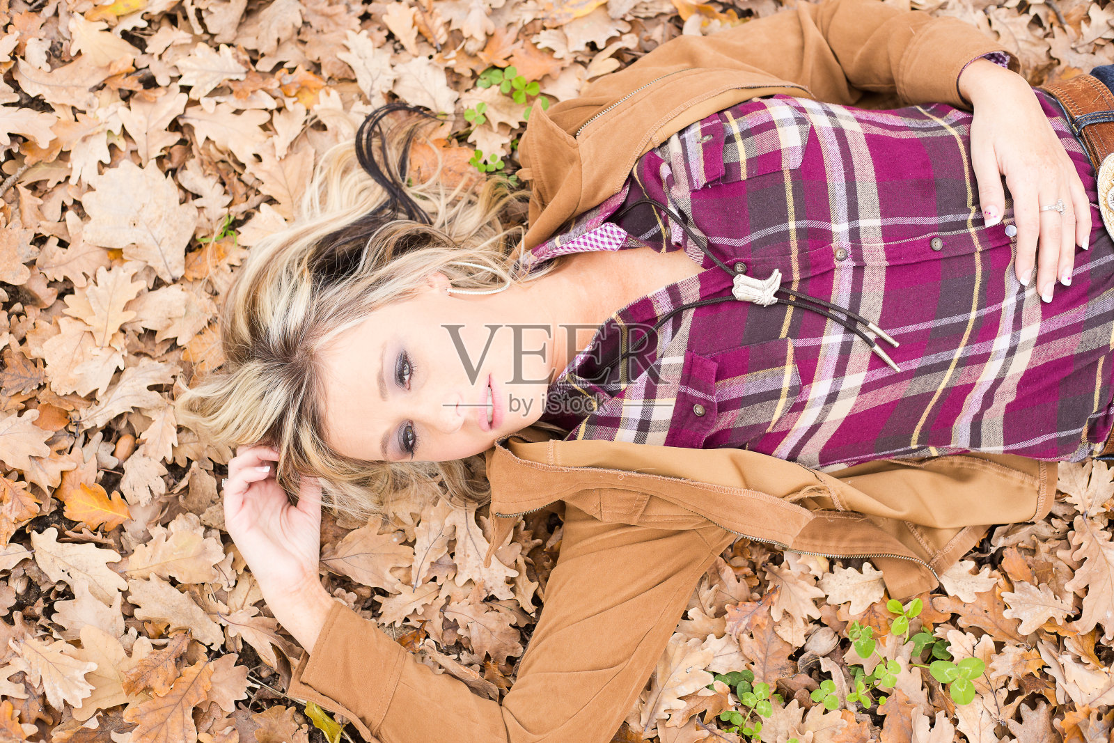 性感的金发农家女孩躺在地上一片干燥的秋天橡树叶上照片摄影图片