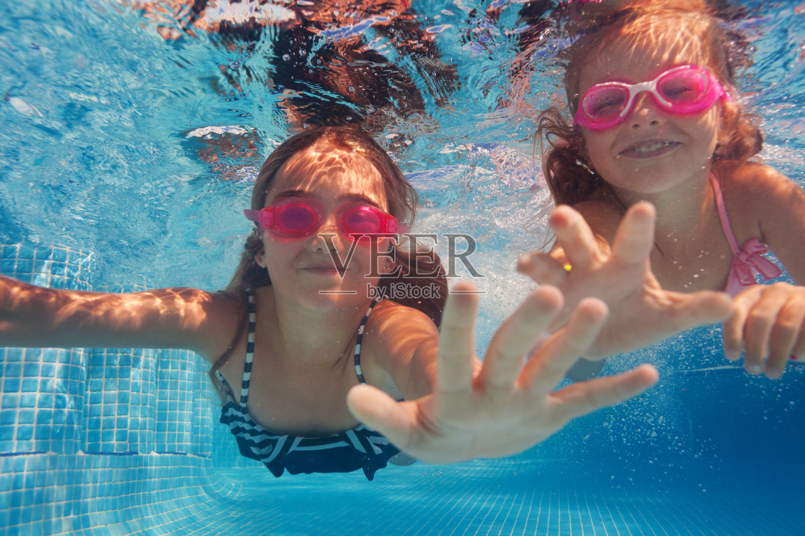 两个快乐的女孩戴着护目镜在水下游泳照片摄影图片