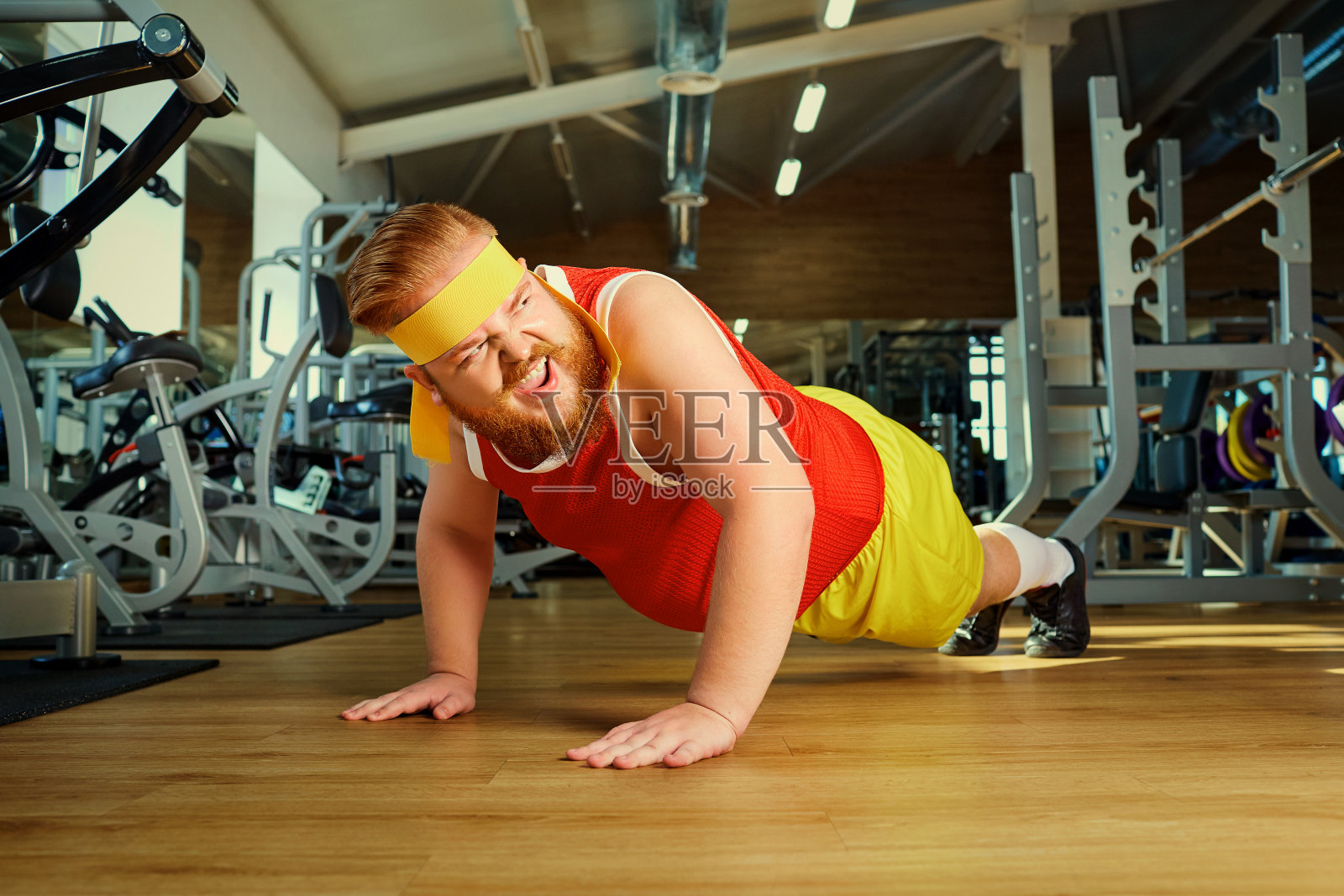 一个胖子在健身房里做俯卧撑。照片摄影图片