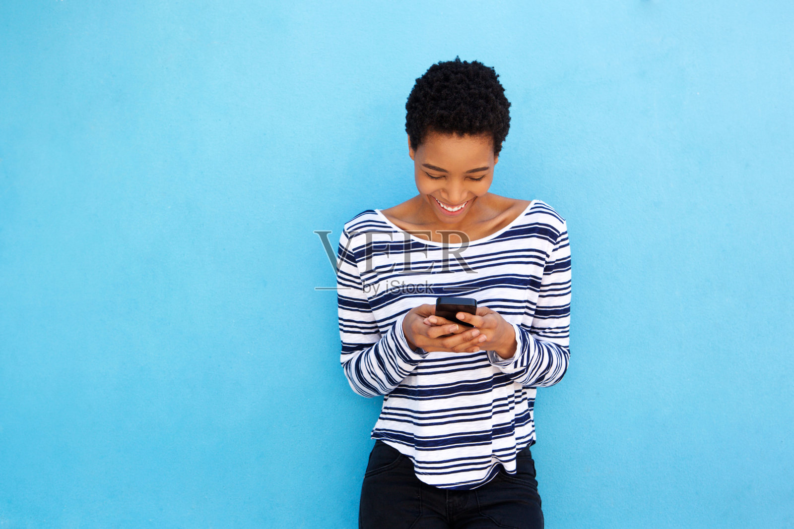 快乐的黑人妇女看着手机在蓝色的背景照片摄影图片