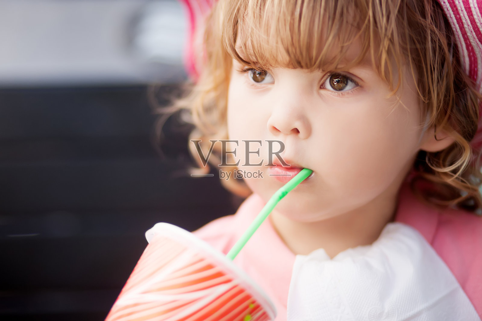 蹒跚学步的小女孩用吸管用玻璃杯喝水。照片摄影图片