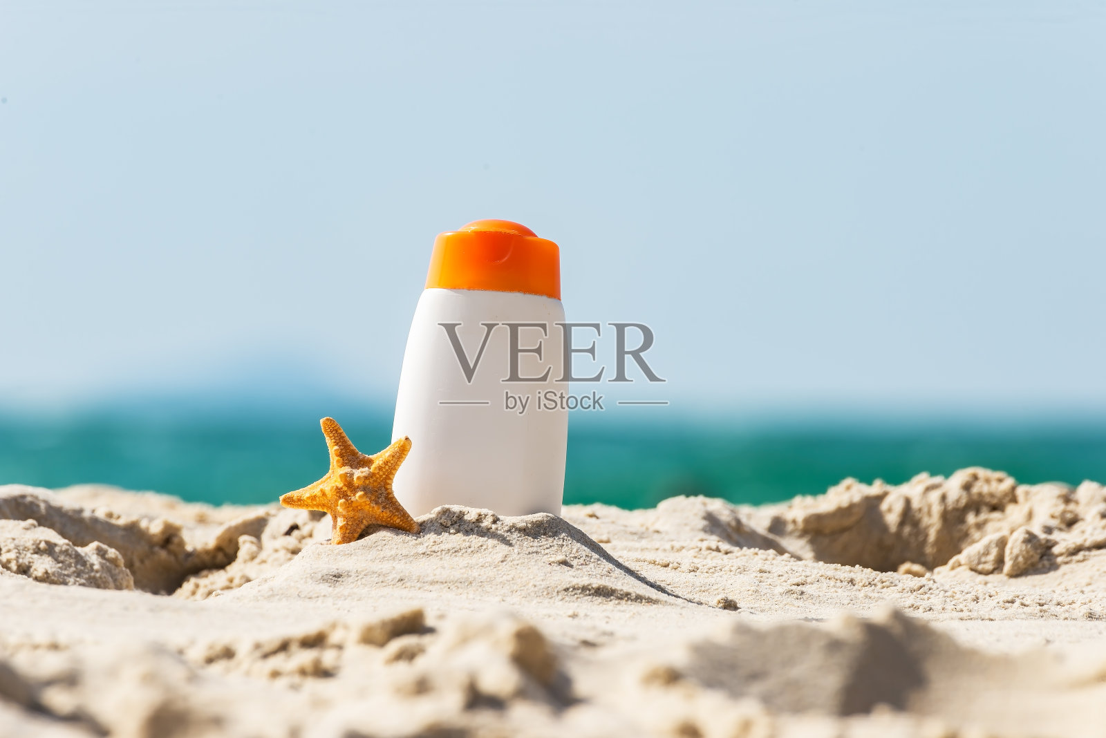 瓶防晒油和海星在热带海滩，海滩配件和夏季概念，拷贝空间。夏天的概念照片摄影图片