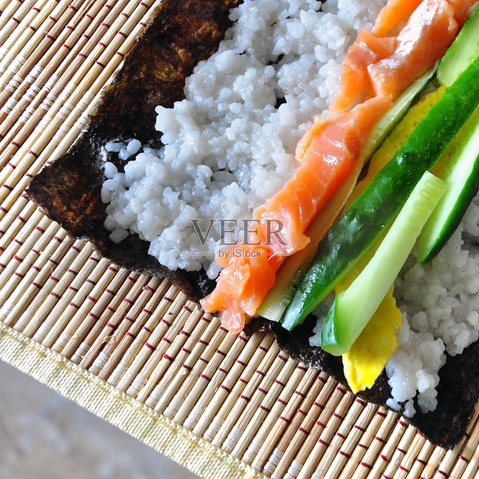自制寿司的过程。海苔、米饭、红鱼、黄瓜、鸡蛋都铺在木质餐巾上。从以上观点。照片摄影图片