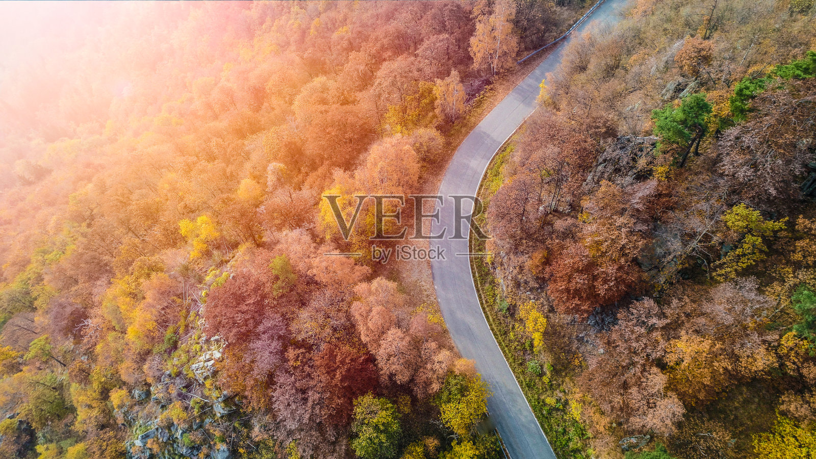 空中鸟瞰图在弯曲的道路弯曲在多彩的乡村秋天的森林。秋天有橙色、绿色、黄色、红色的树林和阳光。山转街径背景。笔直的以上观点照片摄影图片