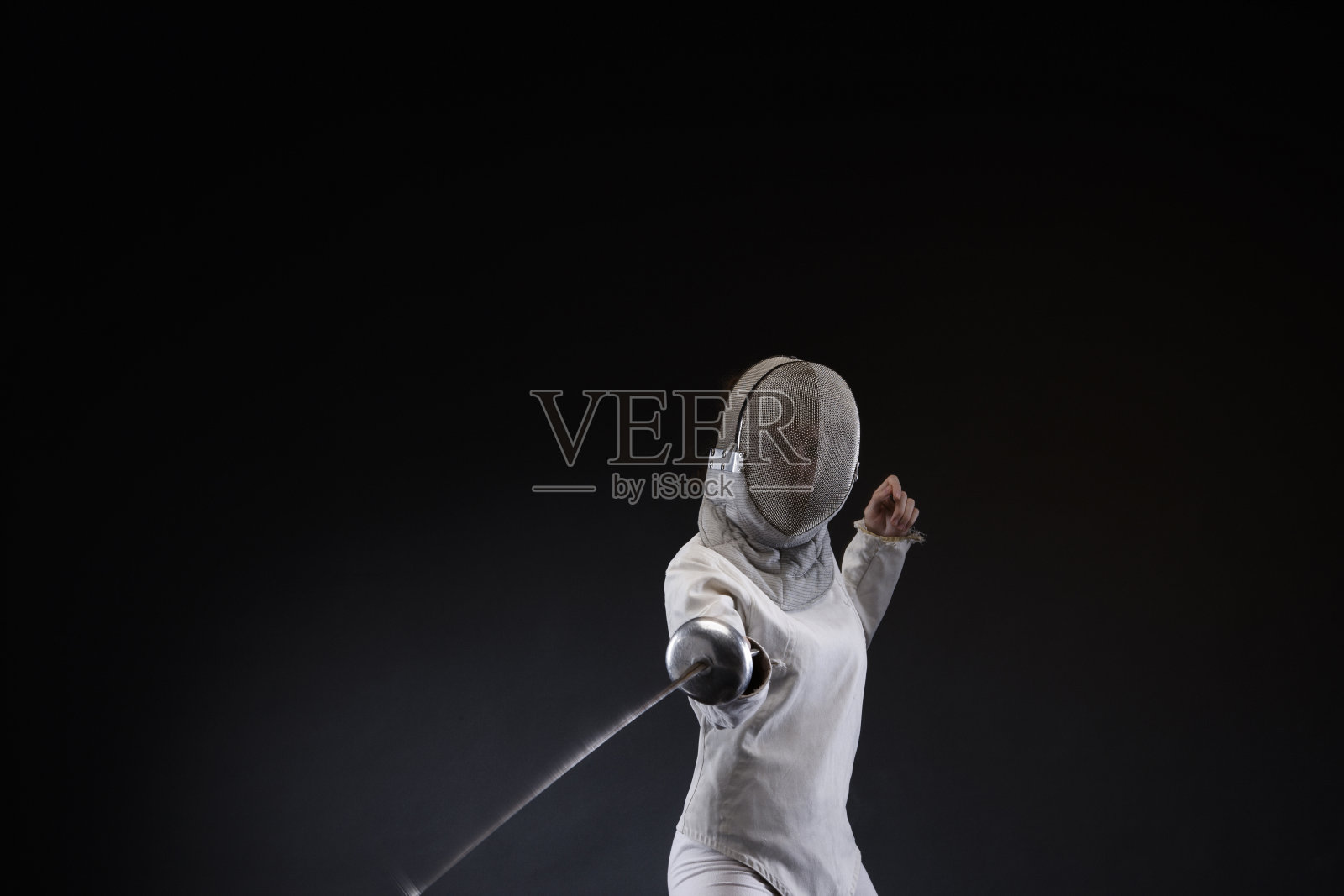 击剑运动在击剑姿势的年轻女子击剑动作。黑色背景。照片摄影图片