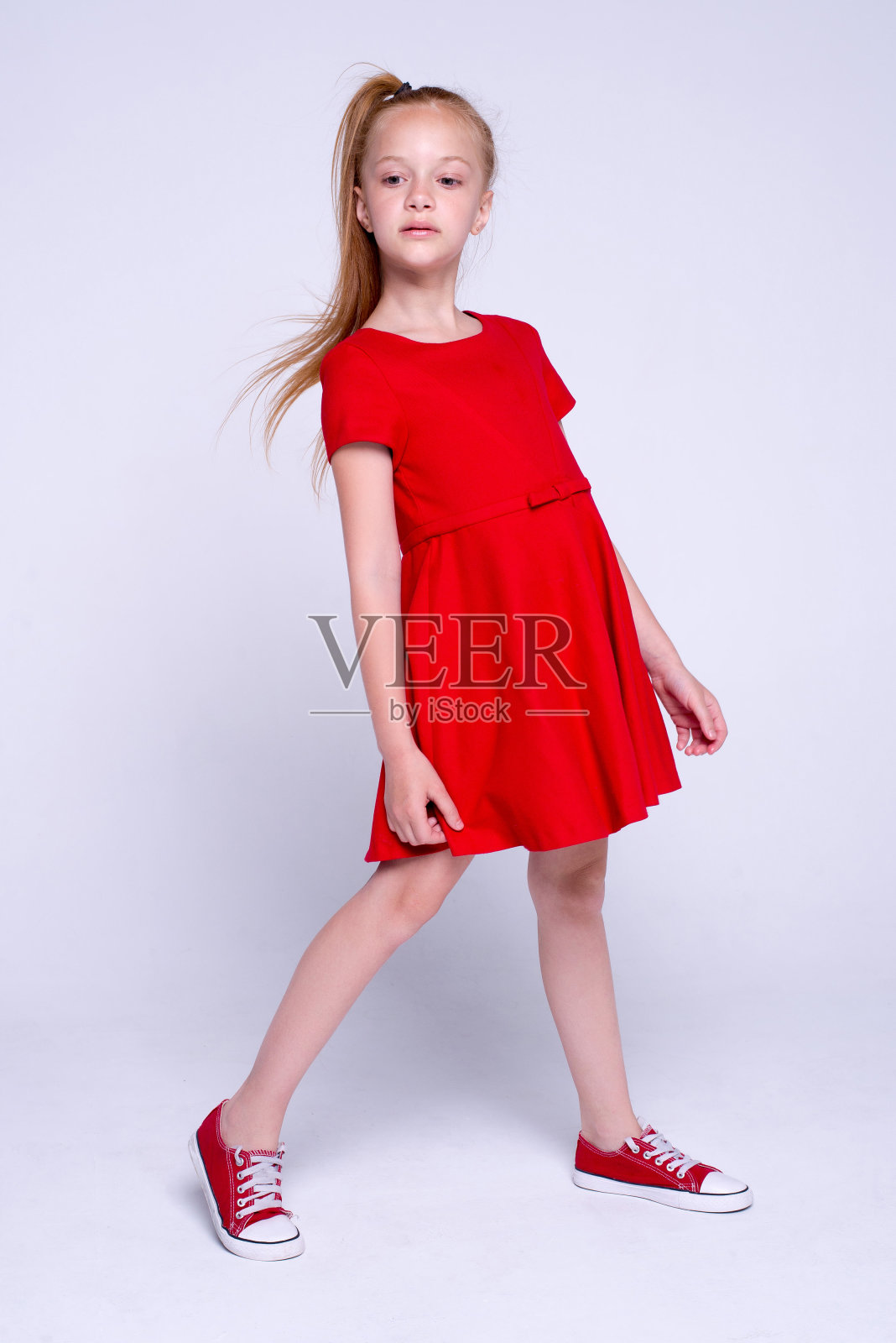 美丽的小红发女孩在红色的裙子和运动鞋摆姿势像模特在白色的背景。照片摄影图片