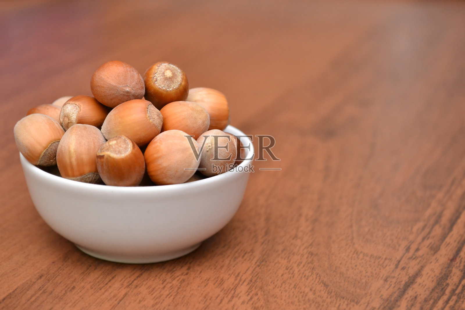 木桌上白色盘子里的坚果。榛子。照片摄影图片