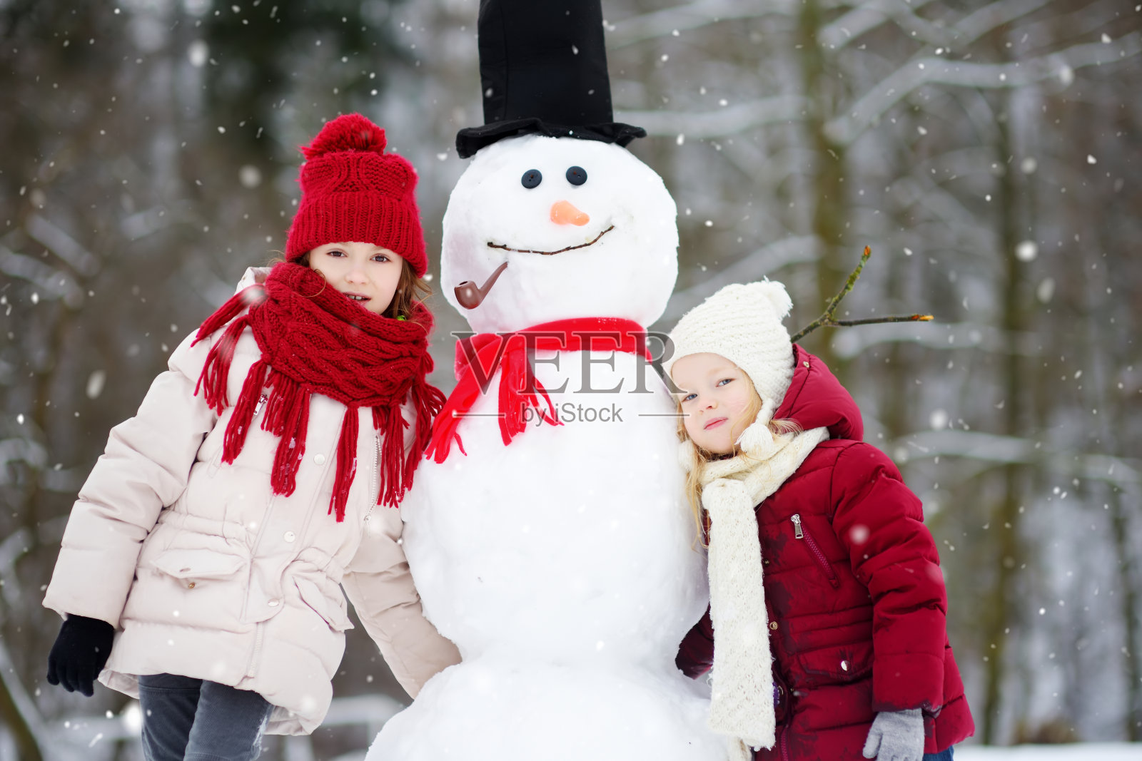 两个可爱的小女孩在美丽的冬季公园里一起堆雪人。可爱的姐妹们在雪地里玩耍。照片摄影图片