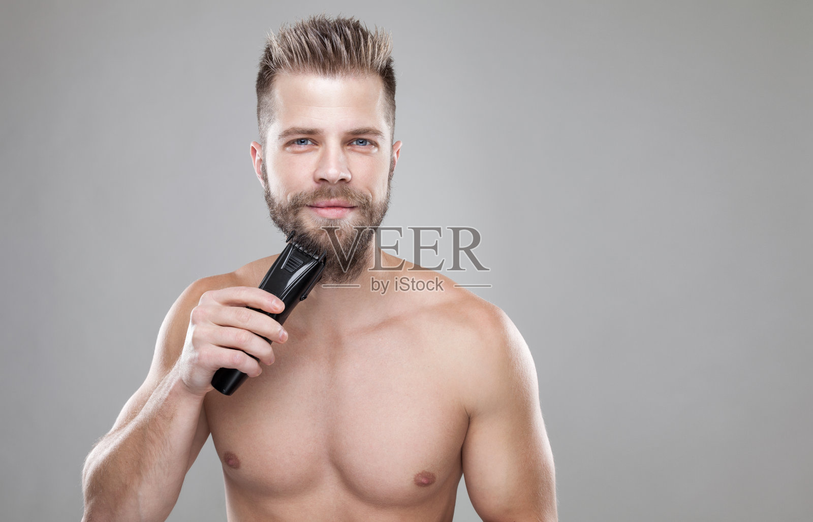 英俊的蓄胡须的男人正在用修胡子机修胡子照片摄影图片