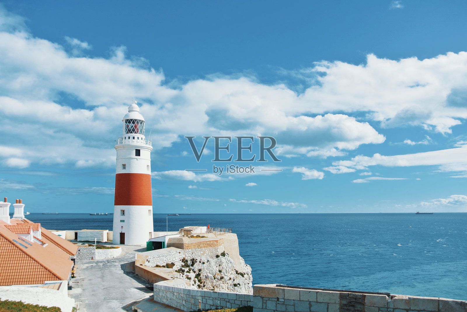 英国，直布罗陀，地中海和大西洋的交汇处，美丽的红白三位一体灯塔，橙色的瓦片屋顶和生动的蓝色海水。照片摄影图片
