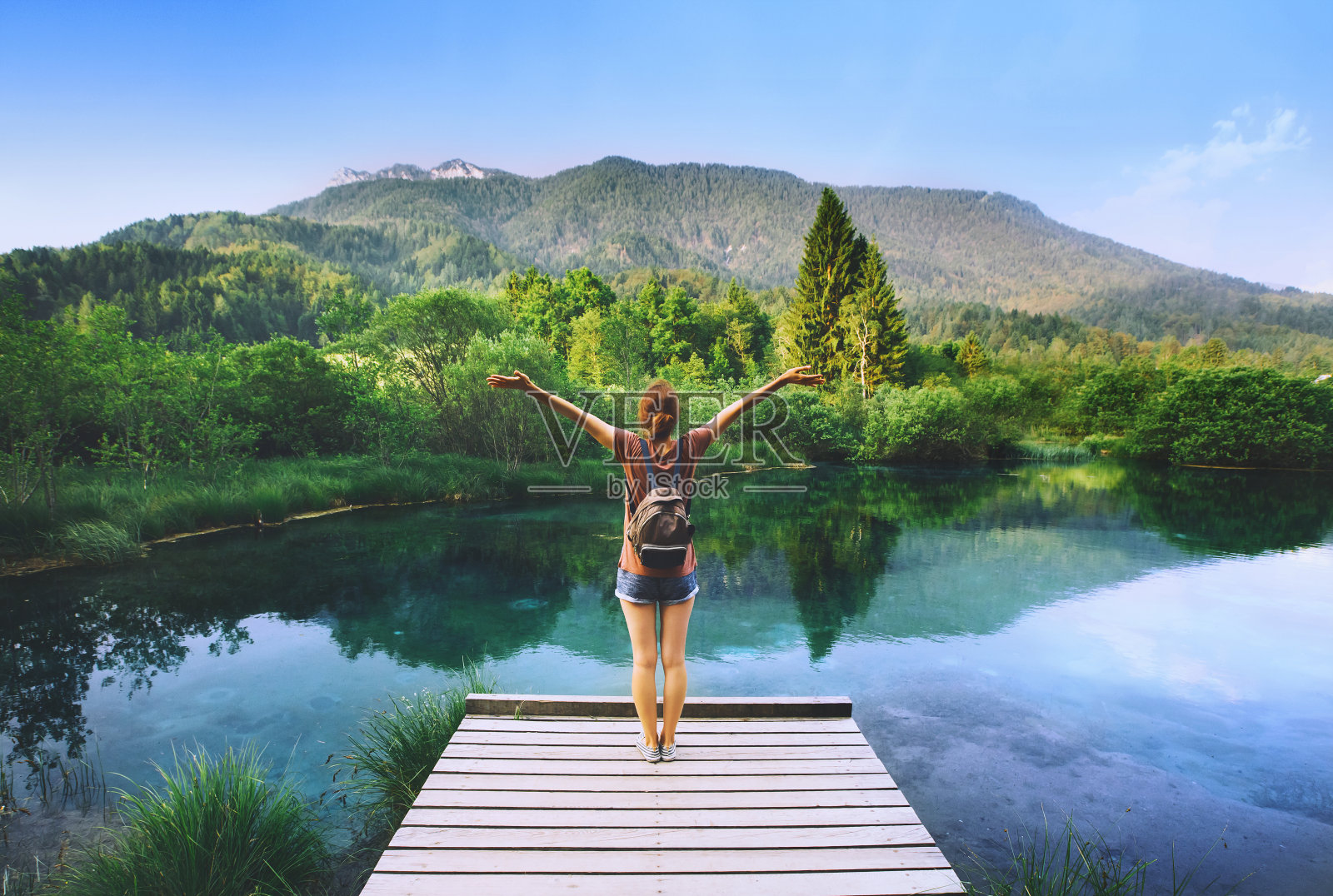 一名年轻女子站在木桥上，双手高举，背景是大自然。照片摄影图片
