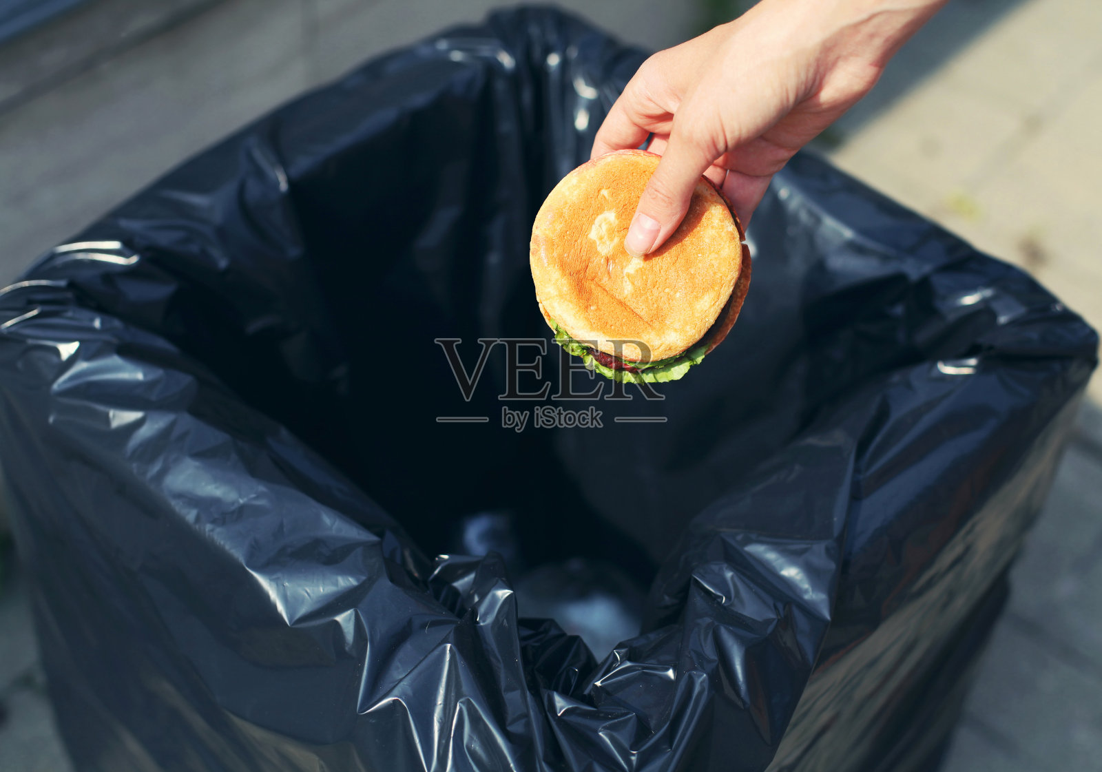 快餐和不健康的饮食概念-手扔一个汉堡在街上的垃圾桶照片摄影图片