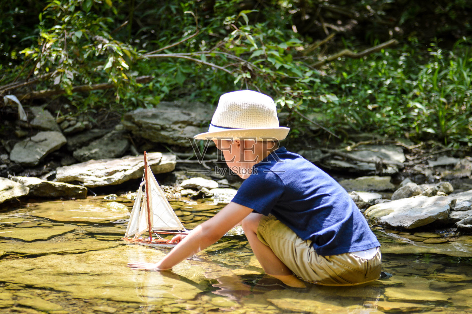 夏天，小男孩在小溪里玩玩具帆船照片摄影图片