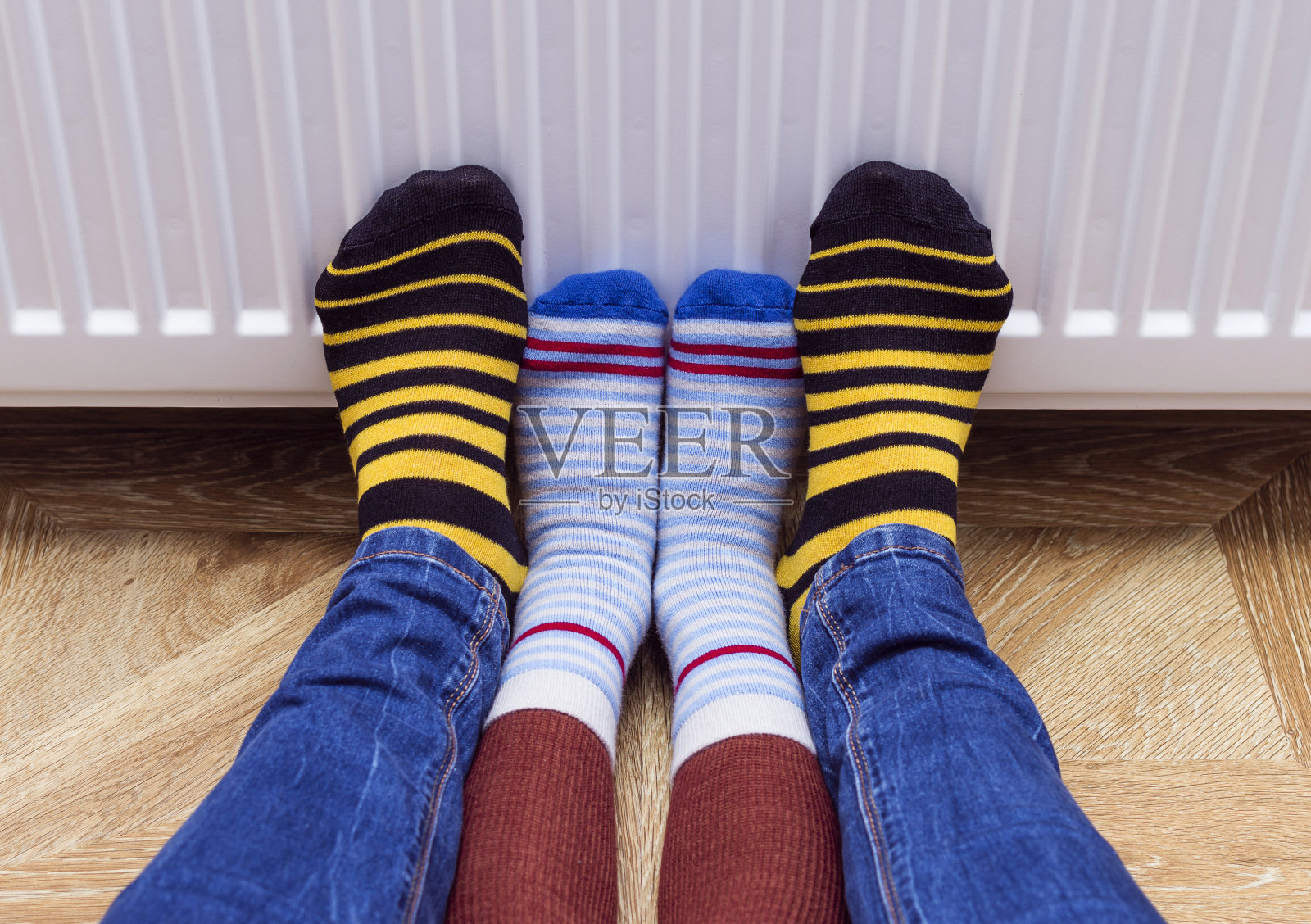 妈妈和她的儿子穿着一双彩色的袜子在暖气片前暖脚。家用燃气或电加热器。有选择性的重点。照片摄影图片