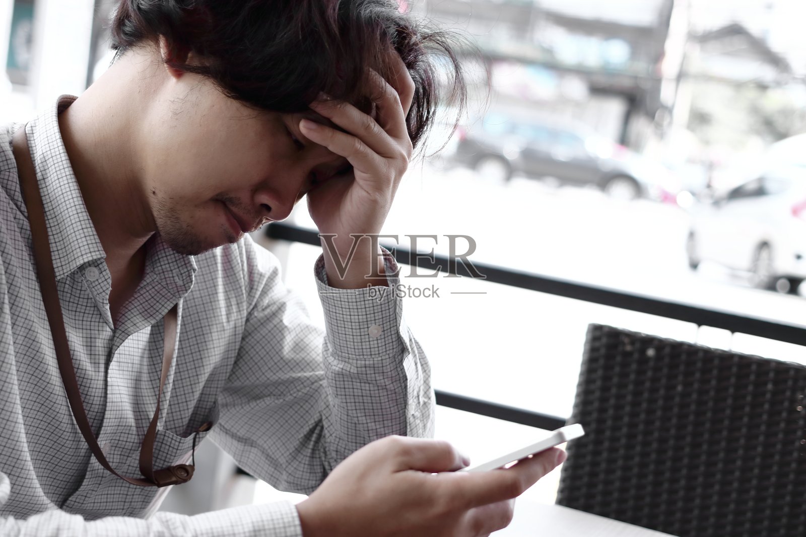 愁眉苦脸的年轻亚洲商人看着手机。焦虑的业务概念。照片摄影图片