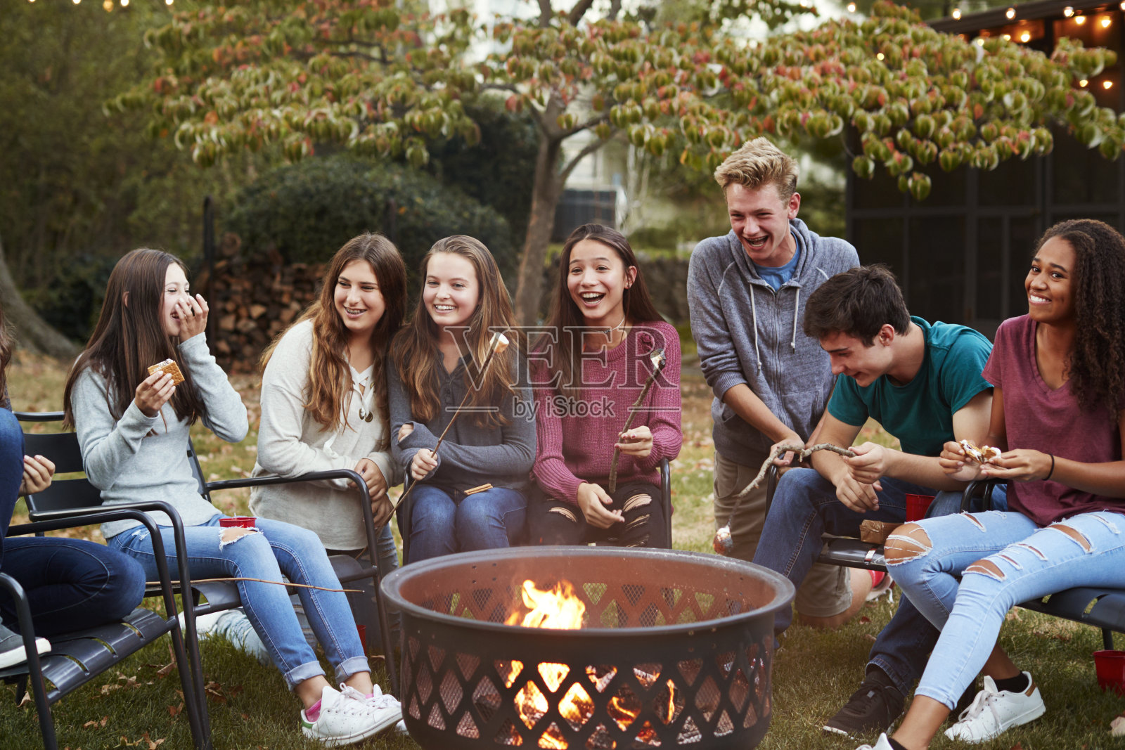 十几岁的朋友围坐在火坑旁烤棉花糖照片摄影图片