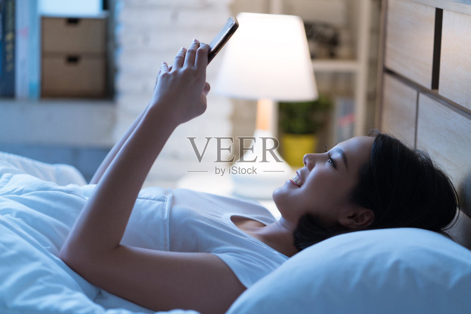 亚洲女性晚上睡觉前会在床上使用智能手机。手机成瘾的概念。照片摄影图片