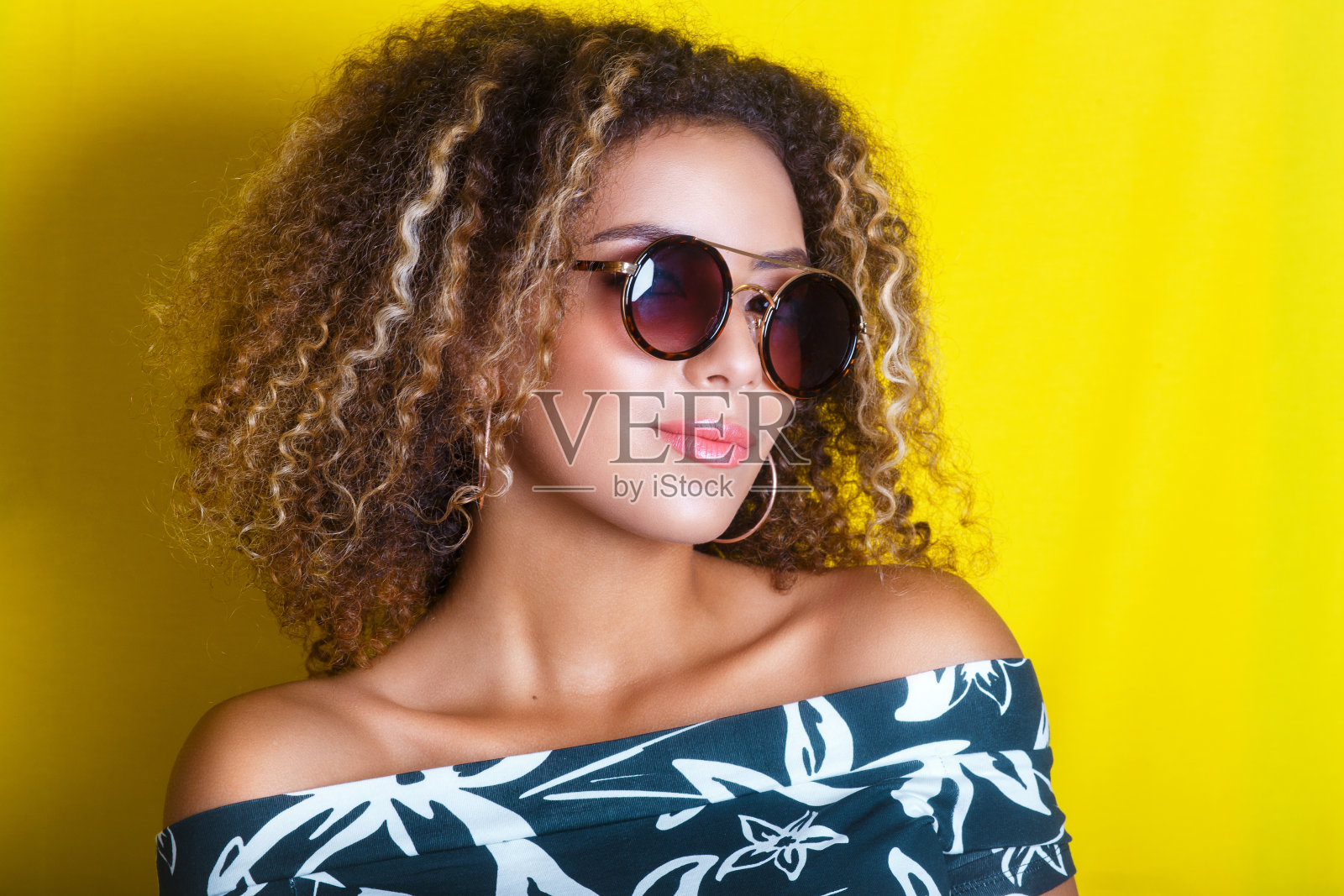 一位戴着太阳镜的年轻美国黑人妇女的室内肖像。黄色背景。的生活方式。休闲装照片摄影图片