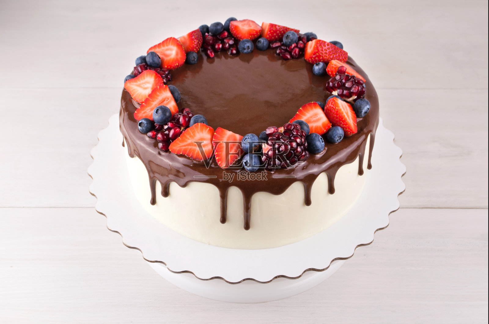白色木桌上放着巧克力蛋糕，草莓、蓝莓和石榴。照片摄影图片