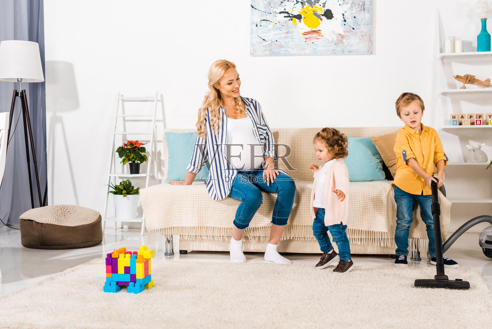 微笑的孕妇看着可爱的孩子打扫房间用吸尘器在家照片摄影图片