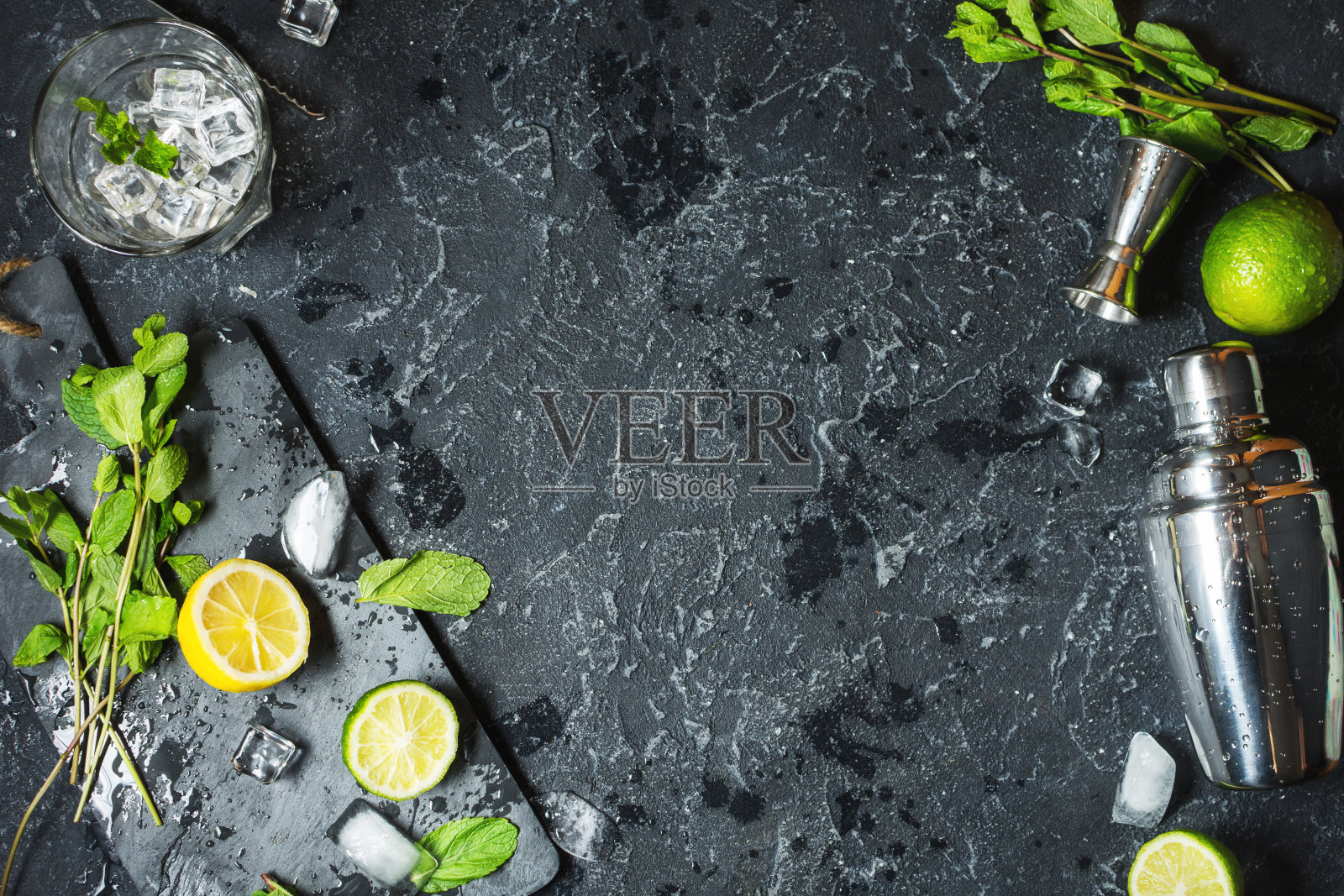 莫吉托鸡尾酒。薄荷，酸橙，玻璃，冰块，配料和摇酒器在黑色的石头背景照片摄影图片