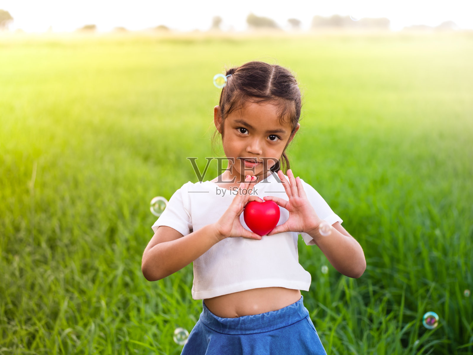 亚洲小女孩的肖像抱着红色的心。照片摄影图片