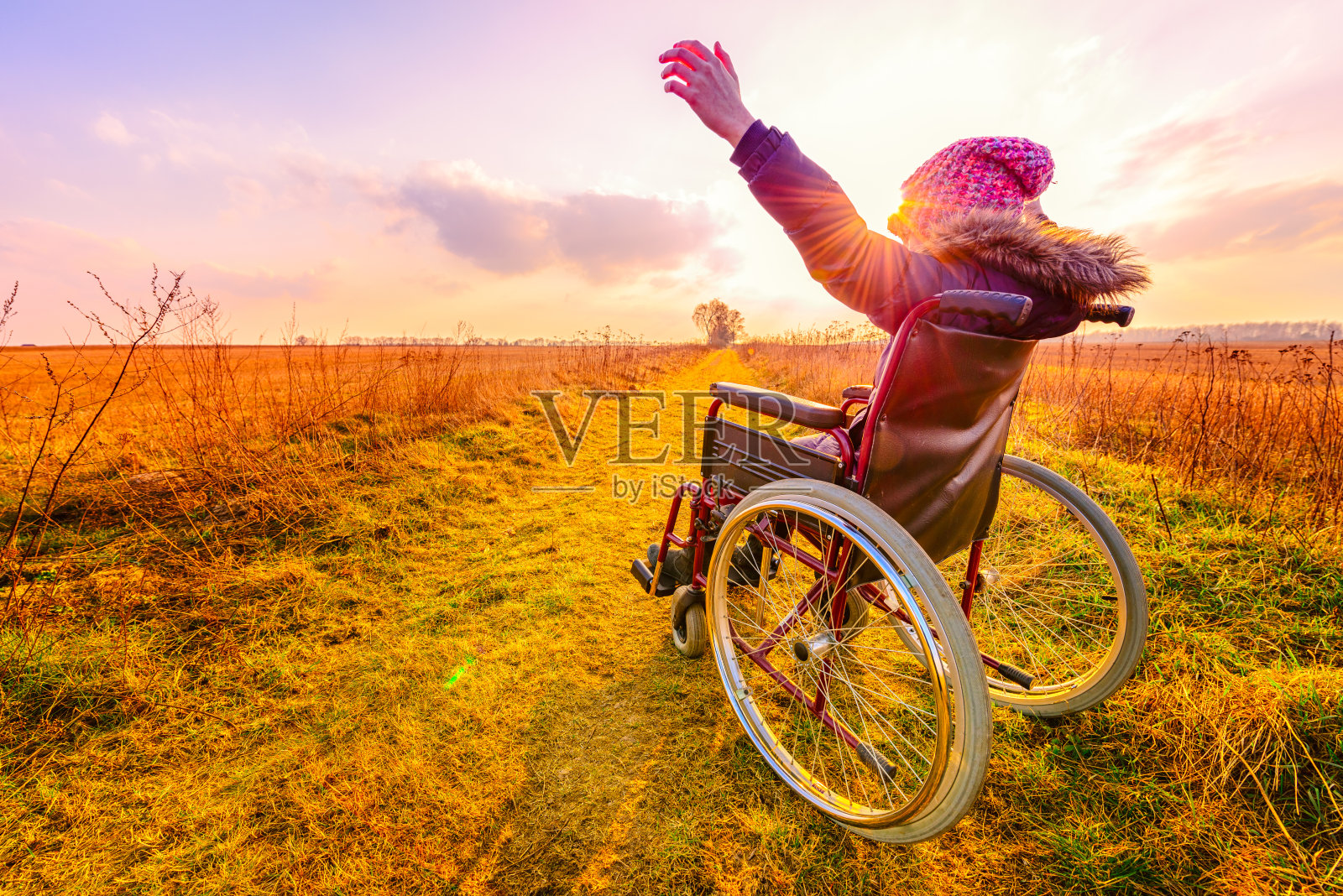 日落时的快乐女人。一个小女孩坐在轮椅后座上照片摄影图片