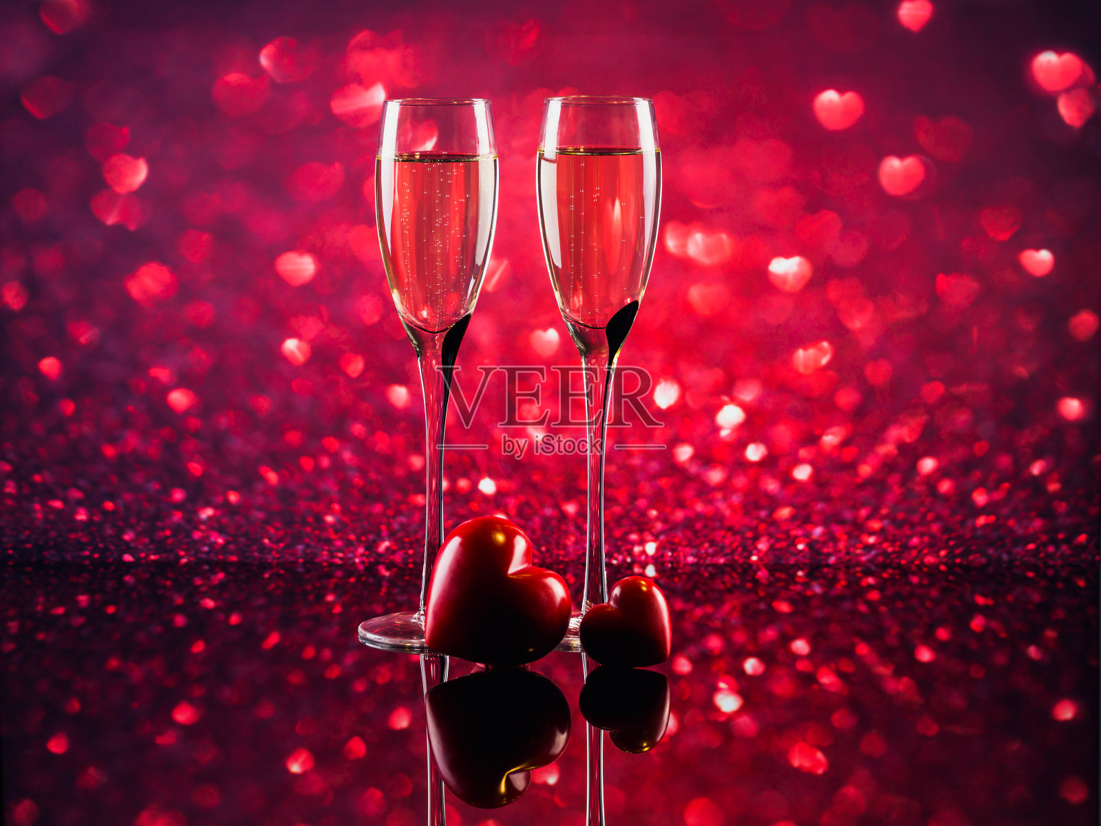 两杯香槟和红色的心型焦的背景。照片摄影图片