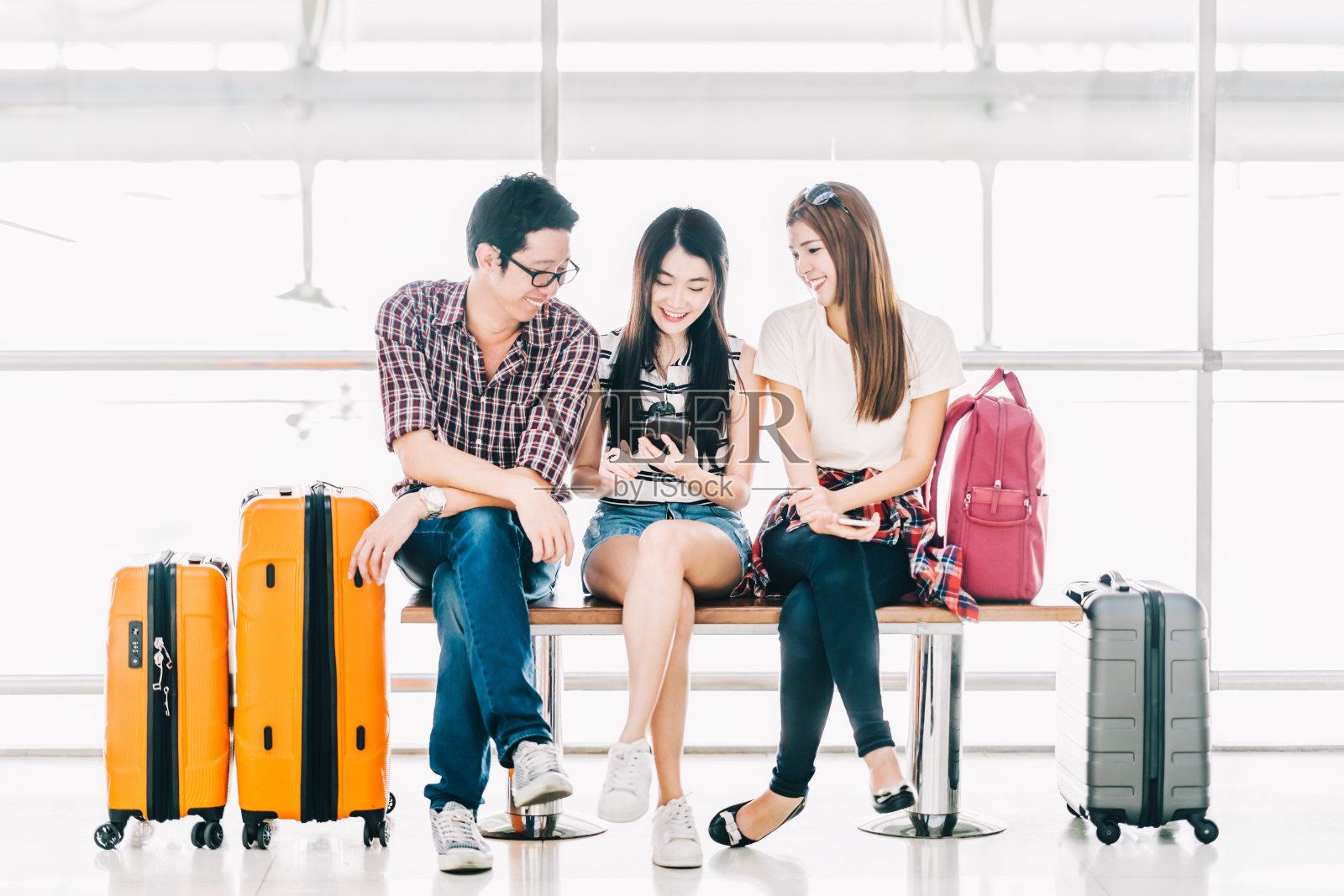 一群年轻的亚洲旅行者使用智能手机和行李一起在机场办理登机手续。出国旅游，暑假旅行，或手机应用技术概念照片摄影图片