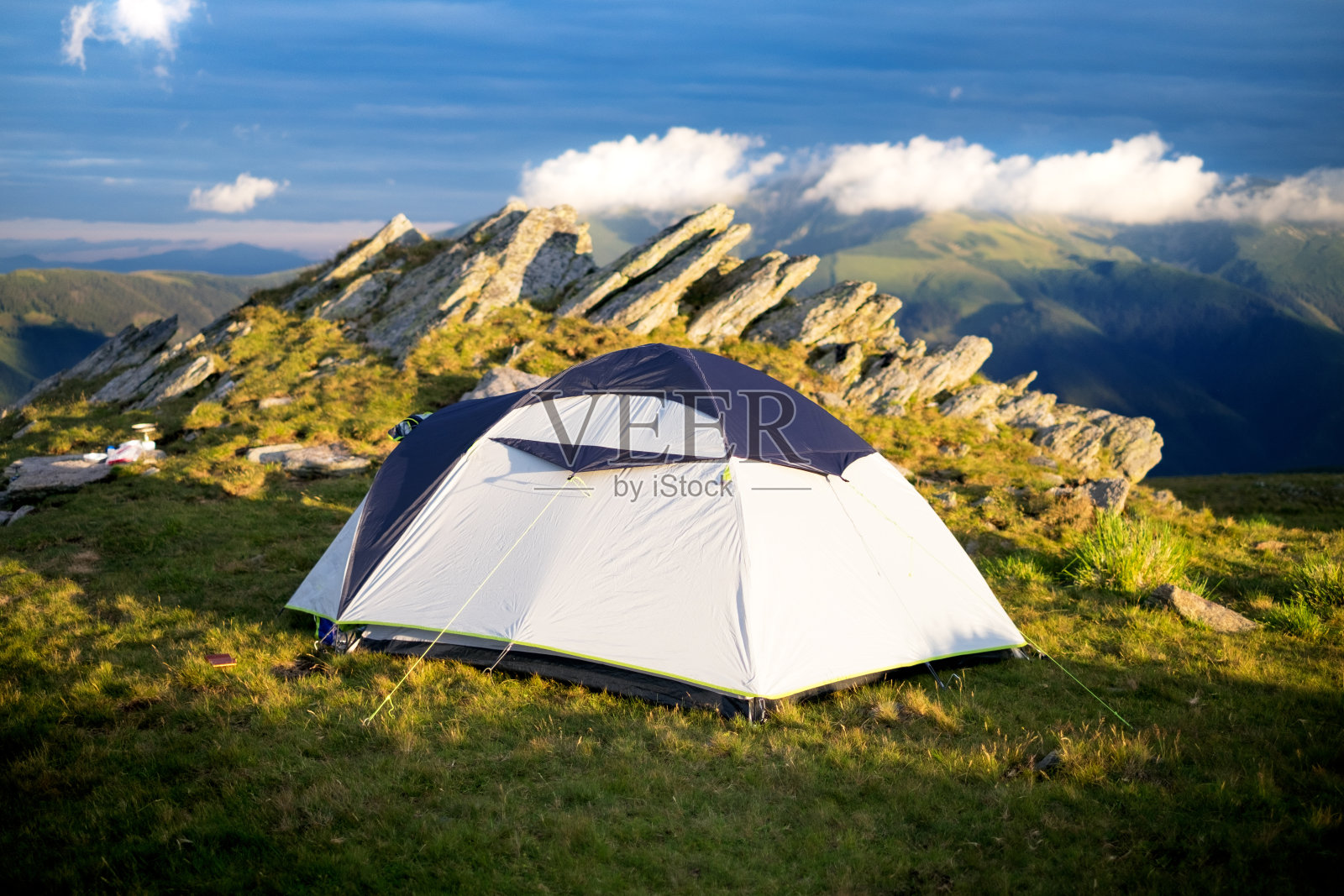 游客在岩石旁边的草地上搭帐篷。山上的帐篷。日落。假期和夏季时间。照片摄影图片