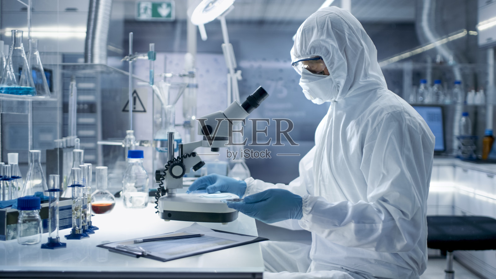 在一个安全的高水平实验室里，科学家们穿着工作服进行一项研究。生物学家用钳子调整培养皿中的样本，并在显微镜下检查它们。照片摄影图片