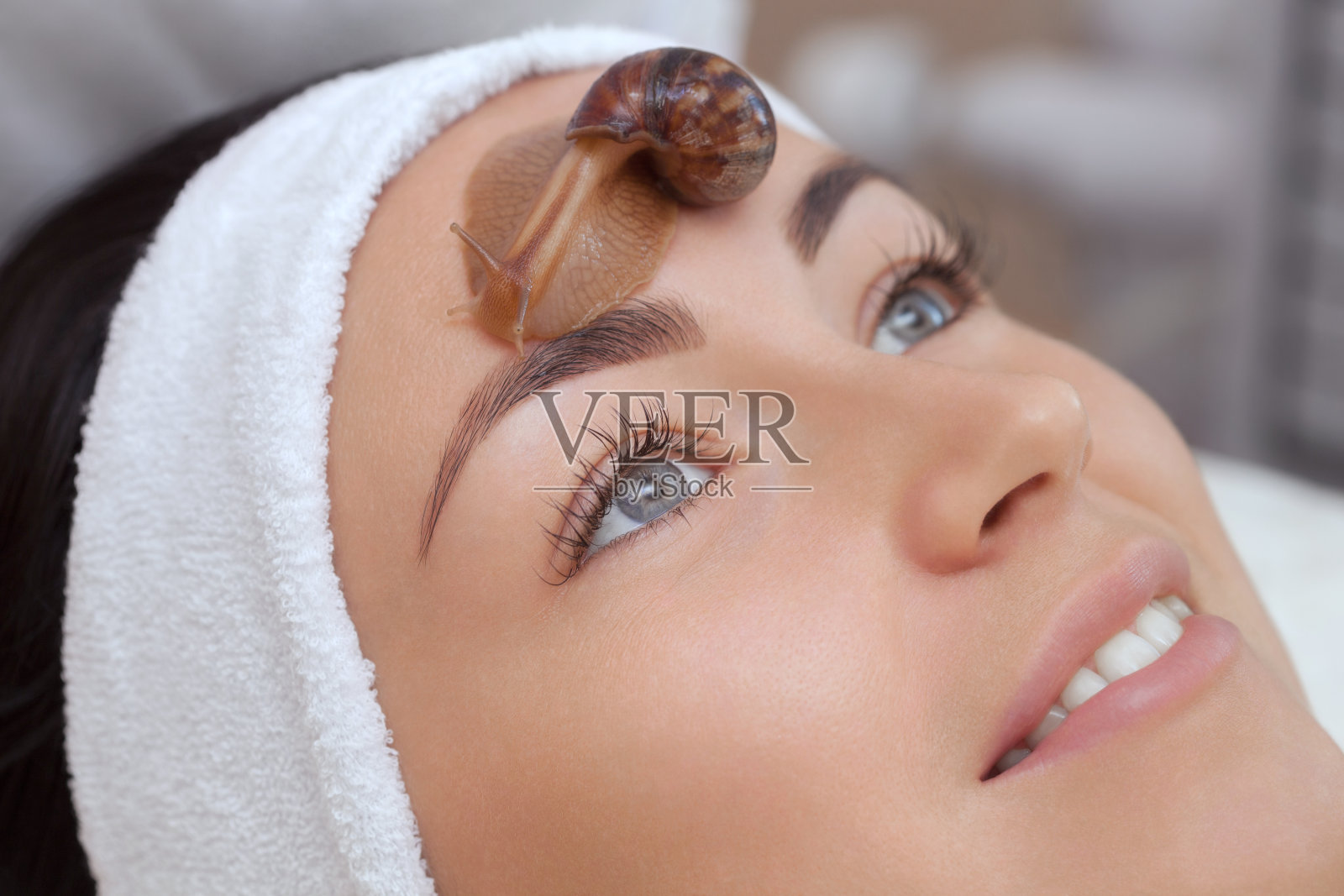 Cosmetological过程。美丽的年轻女子，脸上有个蜗牛状的头巾照片摄影图片