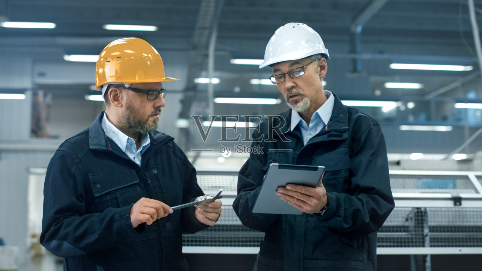 站在工厂里，两位工程师戴着安全帽在平板电脑上讨论信息。照片摄影图片