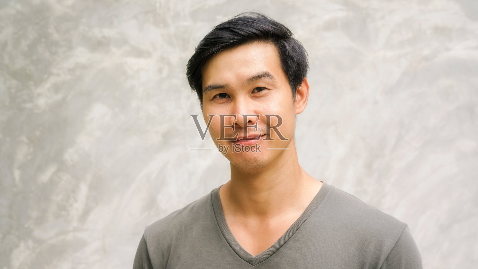 一个亚洲年轻人在灰色的背景上微笑。照片摄影图片